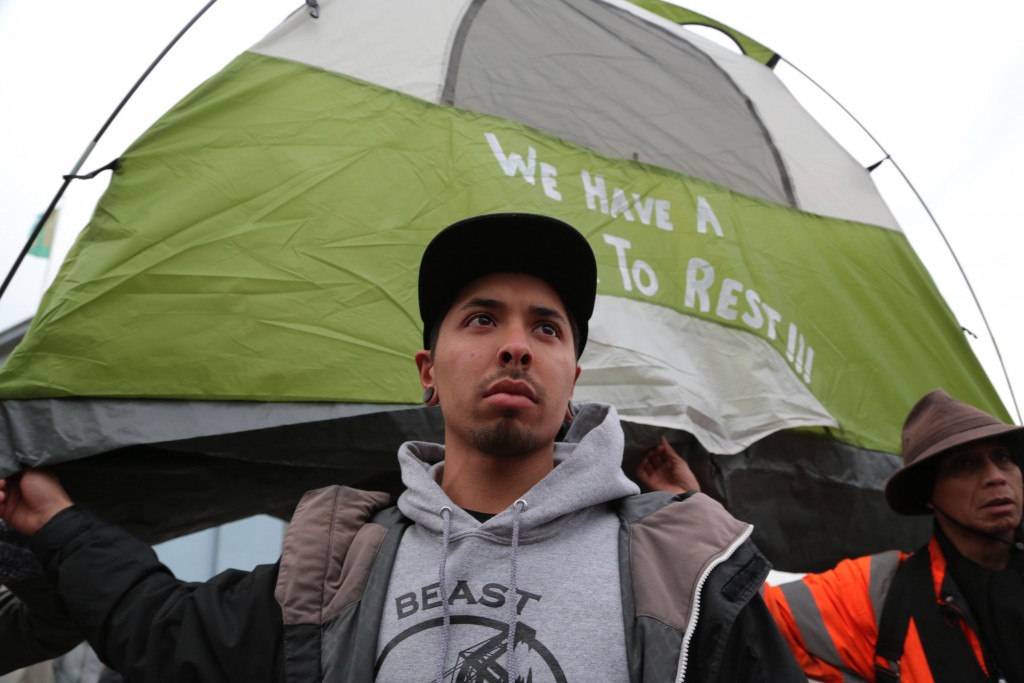 Angelo Chavez holds up a tent to prevent from being cited by police officers during a protest outside Super Bowl City. (Photo by Gabriella Angotti-Jones)