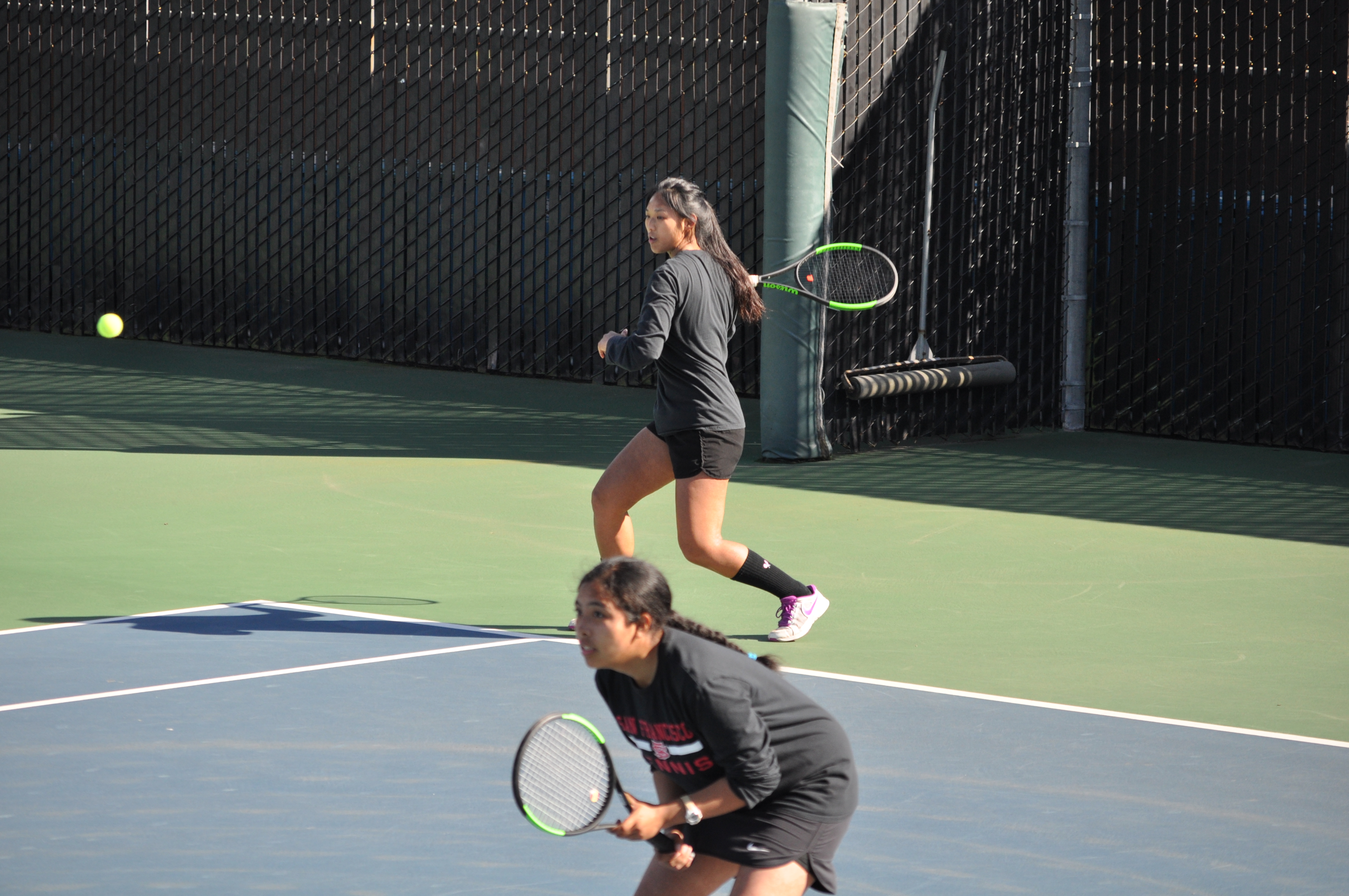 Sophomore Yvonee Ng (right) serves during doubles play with Abigail Campos (left) against Cabrillo College on March 16, 2018. Photo by Peter J. Suter/The Guardsman.