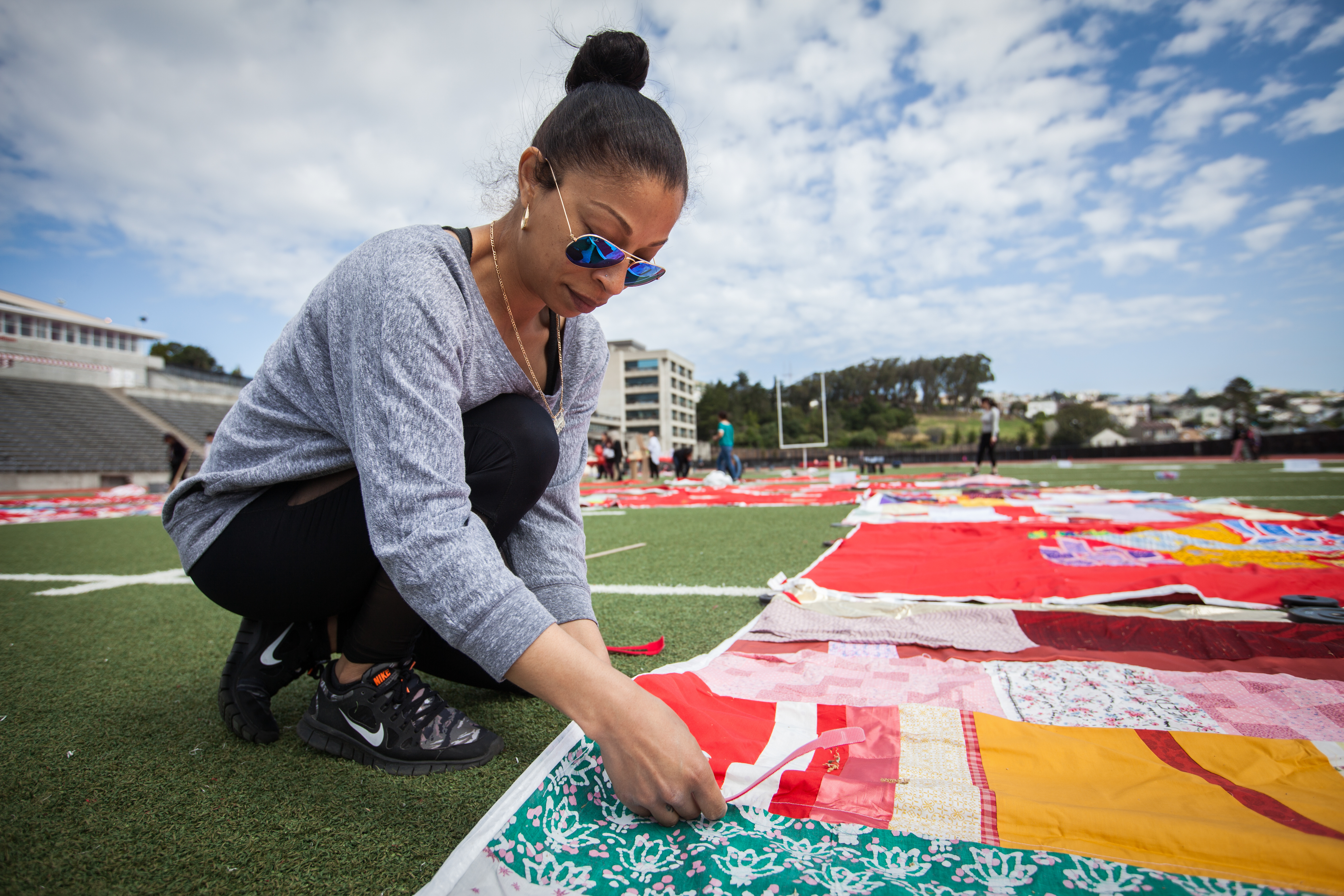 A volunteer, Alexis Ortiz, City College of San Francisco Women’s Studies student helps set up during the installation of The Monument Quilt on the football field of George M. Rush Stadium at City College of San Francisco Ocean Campus on Saturday, May 6, 2017. (Photo by Ekevara Kitpowsong)