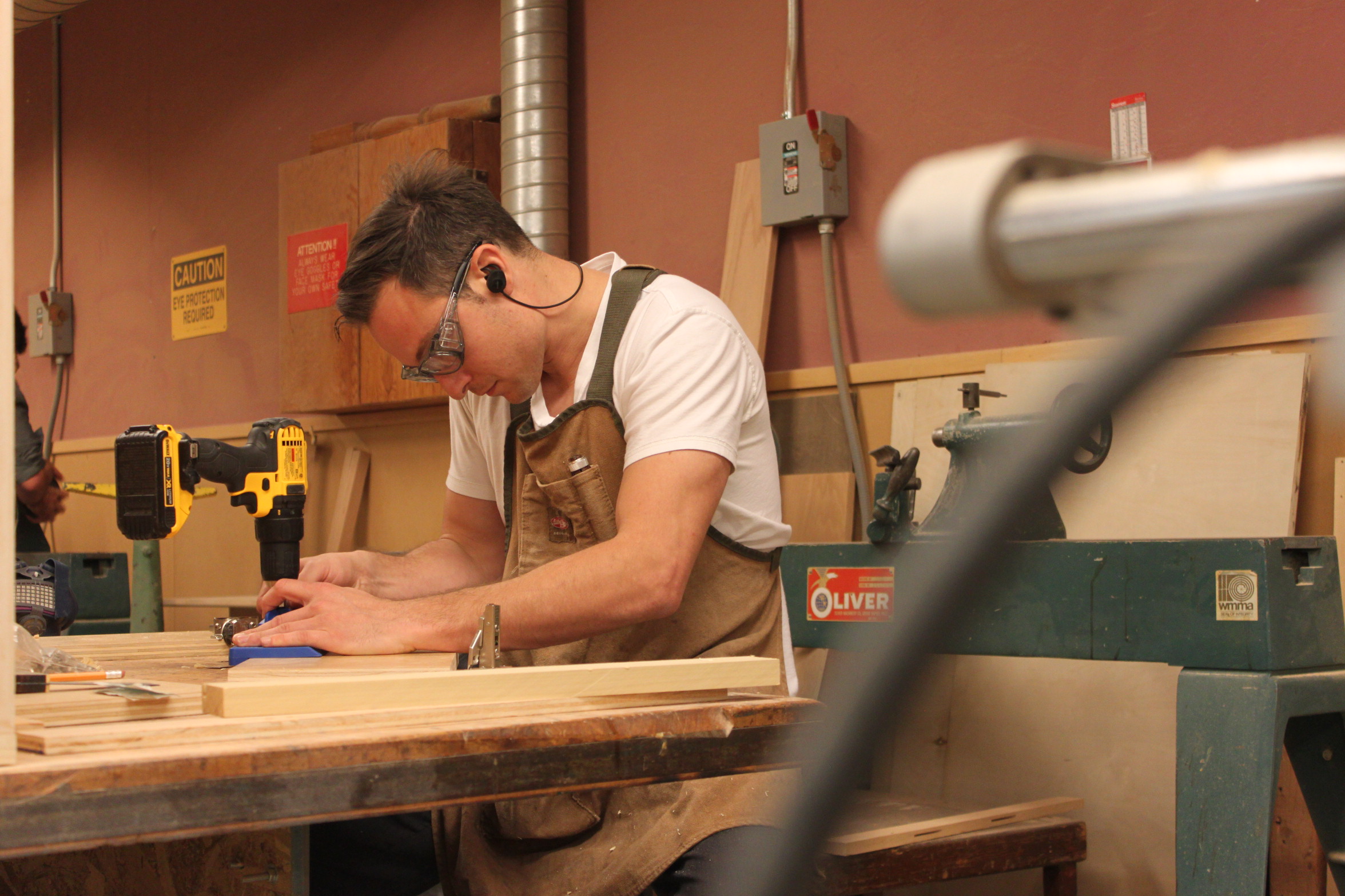 City college student Cem Turhal carefully uses a drill to place hinges on the doors he has crafted for his entertainment center. Turhal has already learned skills from the beginning carpentry class that he uses here. Photo taken by Bethaney Lee on Nov. 6, 2017. 